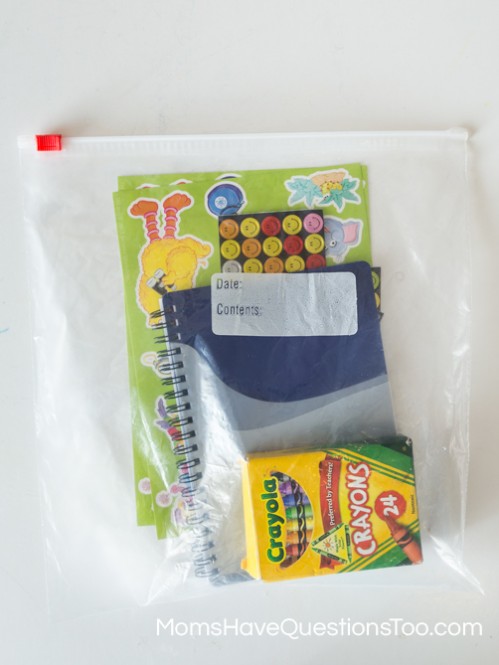 Contents of a simple busy bag for toddlers with paper stickers and crayons - Moms Have Questions Too