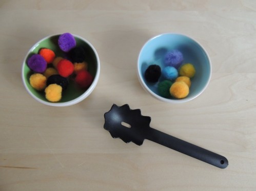 Spoon pompoms from one bowl to another using a kid sized spaghetti spoon