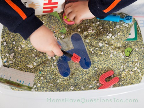H sensory bin. The base is colored sand and a few aquarium rocks. Lots of uppercase and lowercase Hs, plus a hammer, a hat and more.